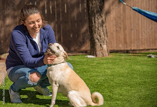 Fototapeta Pretty girl petting a happy white dog with a curly tail in a backyard with a hammock in the background.