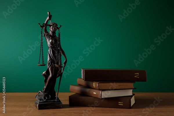Fototapeta bronze statuette with scales of justice and volumes of books on wooden table on dark green background