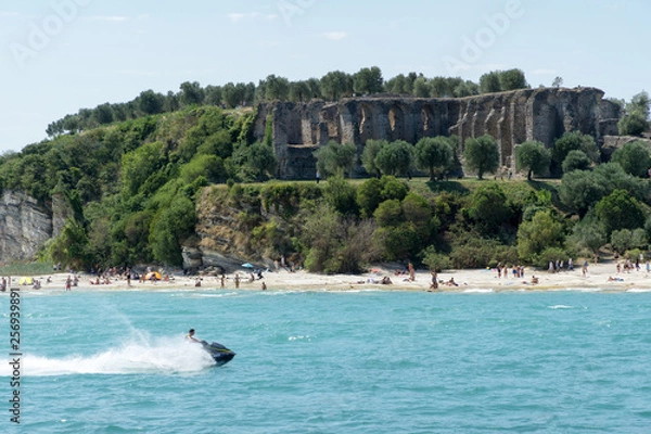 Obraz Stony Beach of Sirmione town on Garda Lake with view of Grottoes of Catullus (Grotte di Catullo), the ruins of a Roman villa built at the end of the 1st century B.C. View from Garda Lake.