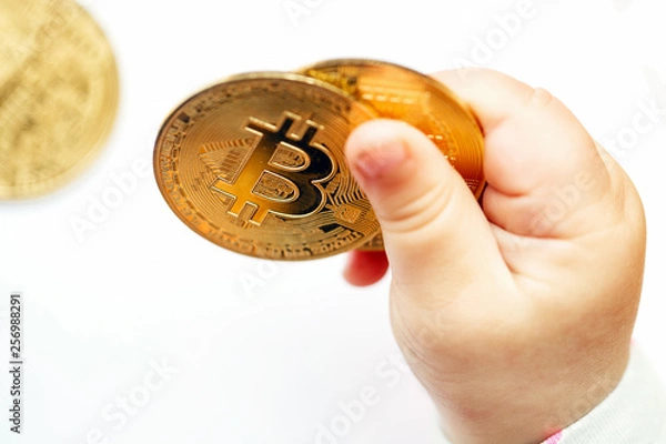Fototapeta The child plays with cryptocurrency. Bitcoin coin in baby hands. Close-up