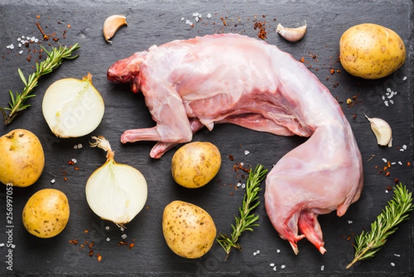 Fototapeta Raw rabbit meat on the black stone board with other ingredients. Selective focus.