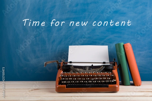 Fototapeta writer's workplace - red typewriter and stationery on blue blackboard background with text "Time for a new content"