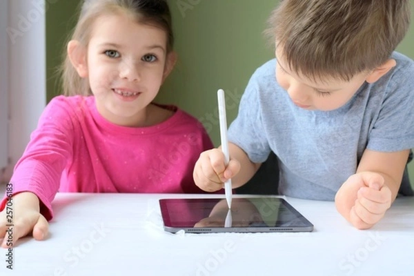 Obraz White caucasian toddler boy and beautiful girl drawing together on tablet screen. Portrait of a happiness little brother and sister. Children play a computer game on the tablet