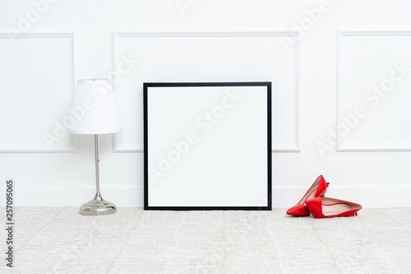 Obraz There are beautiful high heels and various objects near the rectangle blank picture frame in front of white wall on the carpet living room.