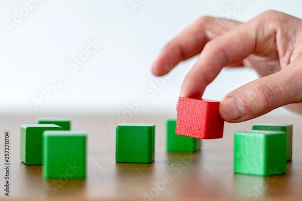Obraz human hand picking up a red wooden cube out of a group of some green cubes