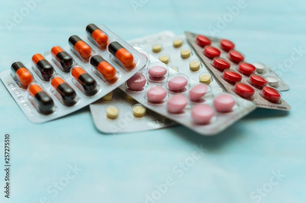 Fototapeta Multicolored pills and capsules in blisters close-up, on blue background. The concept of treating human diseases.