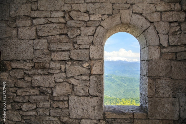 Fototapeta Stone war tower window with motion blurred bird and sea coast view with green tree hills