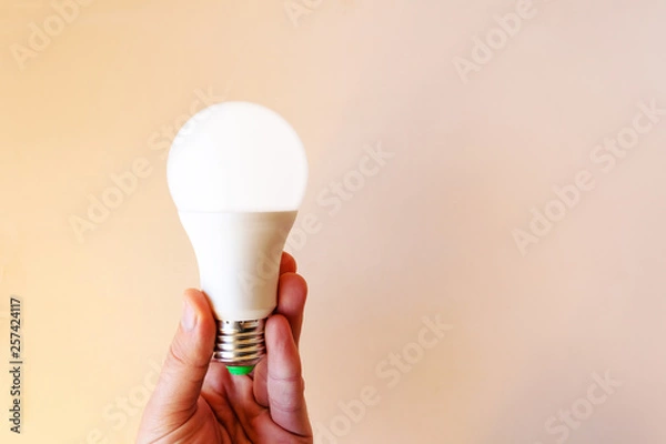 Fototapeta modern bright LED light bulb in hand on a beige background, copy space