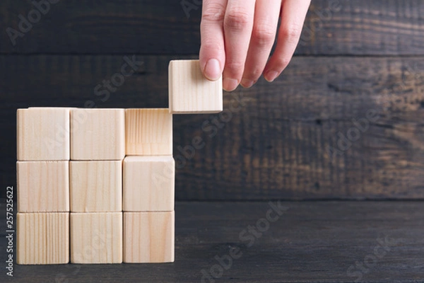 Fototapeta Woman's hand putting the final piece of wooden cube into place - achievement concept. Finish the project concept