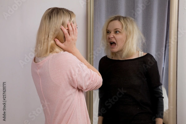 Fototapeta girl looks at herself in the mirror, sees himself in another reflection. The Dark Side, bipolar disorder, dissociative disorder