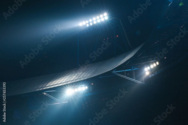 Fototapeta Stadium lights against dark night sky background. Soccer match lights.