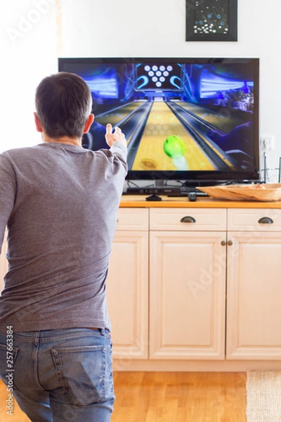 Fototapeta A man playing video game without joystick at home. Cheerful father with family playing bowling and having fun with new trends technology. Gaming concept