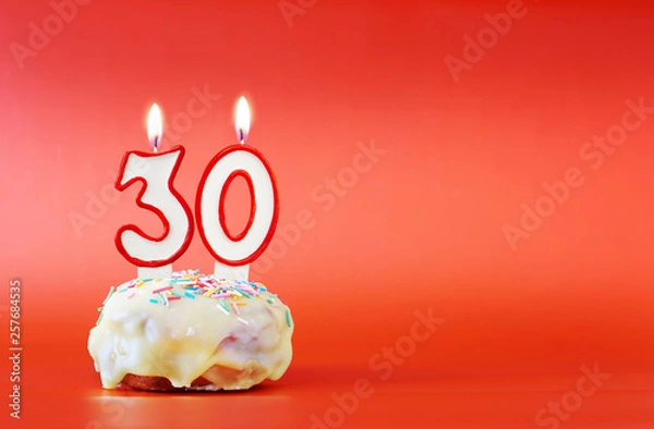 Fototapeta Thirty years birthday. Cupcake with white burning candle in the form of number 30. Vivid red background with copy space