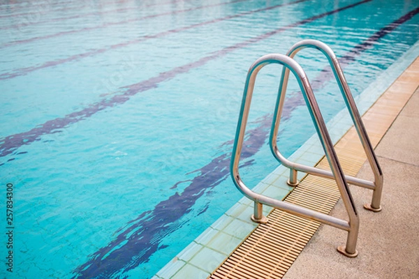Fototapeta Ladder stainless handrails for descent into swimming pool. Swimming pool with handrail . Ladder of a swimming pool. Horizontal shot.