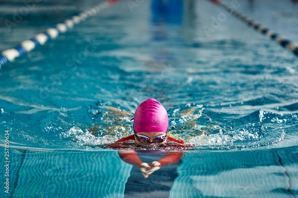 Fototapeta Female athlete in a red-yellow swimsuit is swimming in the style of breaststroke. Splashes of water scatter in different directions.