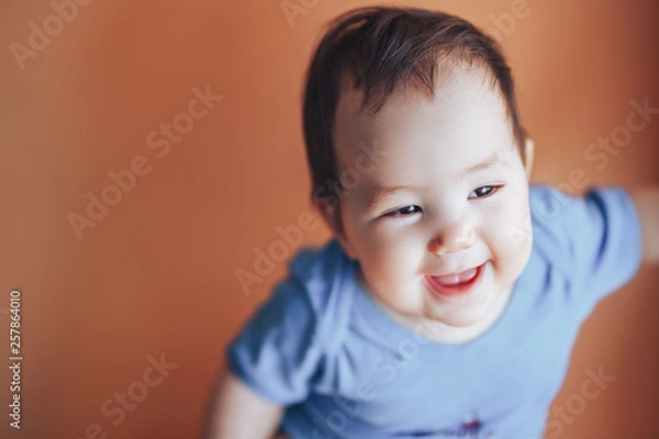 Obraz Beautiful small girl or boy with dark hair smiling on a bright orange background colour of 2019 with space for text happy smile look at camera