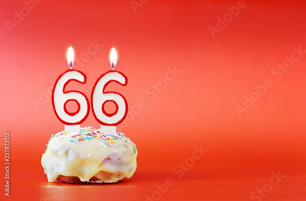 Fototapeta Sixty six years birthday. Cupcake with white burning candle in the form of number 66. Vivid red background with copy space