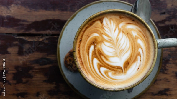 Obraz Top down shot of a perfectly made cappuccino made with locally grown coffee with a latte art rosetta on a worn wooden table framed to the right with a blurry background