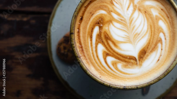 Fototapeta Top down zoomed in shot of a perfectly made cappuccino made with locally grown coffee with a latte art rosetta on a worn wooden table framed to the left with a blurry background