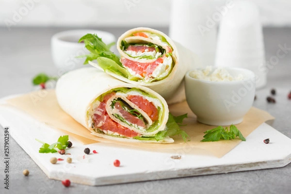 Obraz Tortilla with salmon, lettuce and cream cheese. Delicious snack wraps with fish and salad. Healthy burrito with pita bread for breakfast