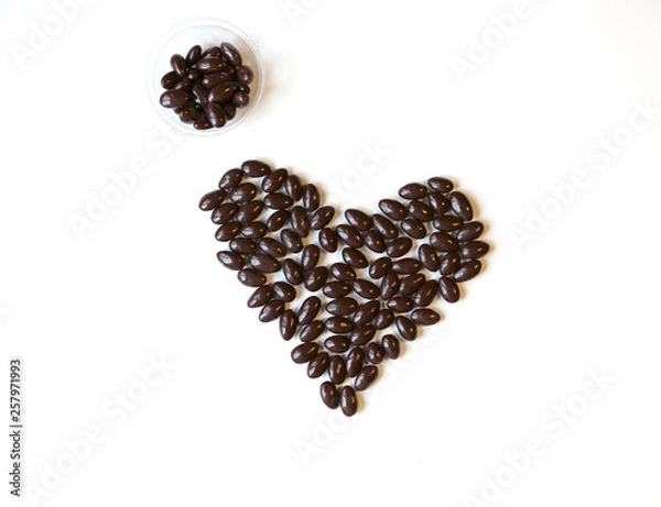 Fototapeta Nuts arranged in heart shape on background. Food image close up candy, chocolate milk, extra dark almond nuts. Love Texture on white grey table top view