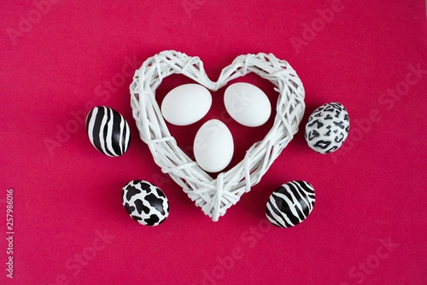 Obraz Easter eggs painted like zebra, cow, snow leopard. Three white eggs inside a white heart on red background. Top view.