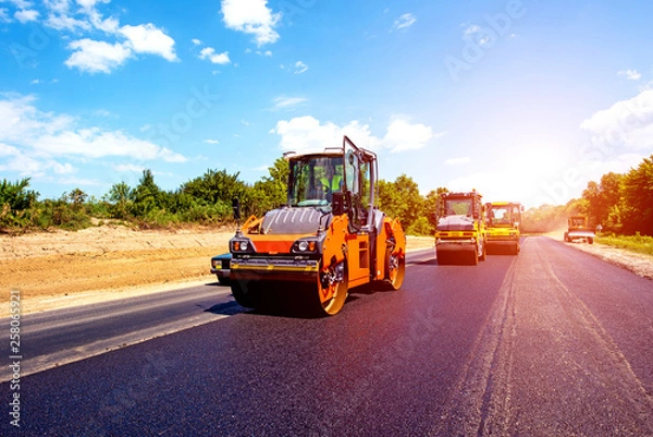 Fototapeta industrial landscape with rollers that rolls a new asphalt in the roadway. Repair, complicated transport movement.