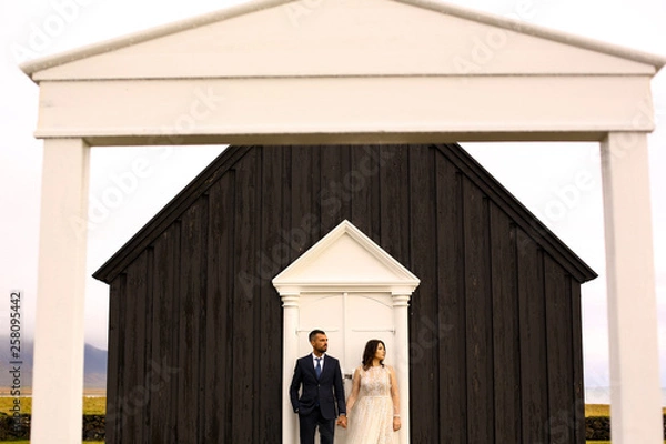 Fototapeta Beautiful wedding couple posing with black old church