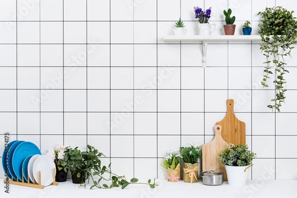 Fototapeta Various kinds of kitchen tools arranged on the white table. And tidy flower pots are placed neatly on the shelf.