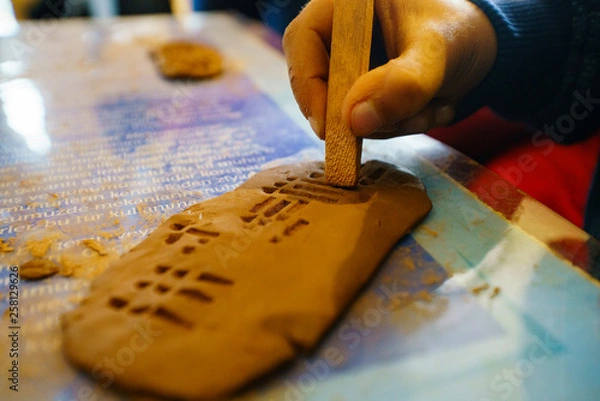 Fototapeta Children education sumerian clay tablet. Ancient type of Akkad empire style cuneiform writing in brown clay with tool. kids education. children education clay