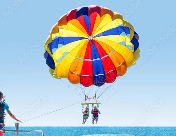 Fototapeta Happy smiling couple Parasailing on Tropical Beach in summer. Newlyweds under parachute hanging mid air. Having fun. Tropical Paradise. Positive human emotions.
