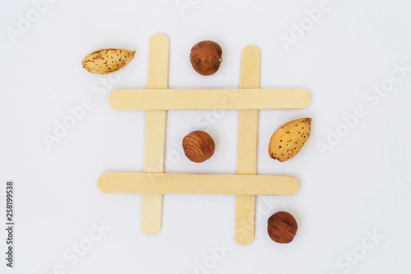 Fototapeta Pistachio nuts and dried fruits on the field for the game of tic-tac-toe on a white background