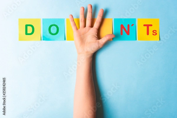 Fototapeta Do's and don'ts sign with multicolored sticky notes and a palm of hand showing 5 fingers on blue background