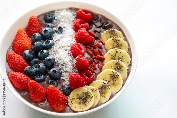 Fototapeta Acai Berry superfoods smoothies white bowl with chia seeds, strawberry, goji berry, coconut, blueberry, raspberry toppings, and chocolate chip on white background