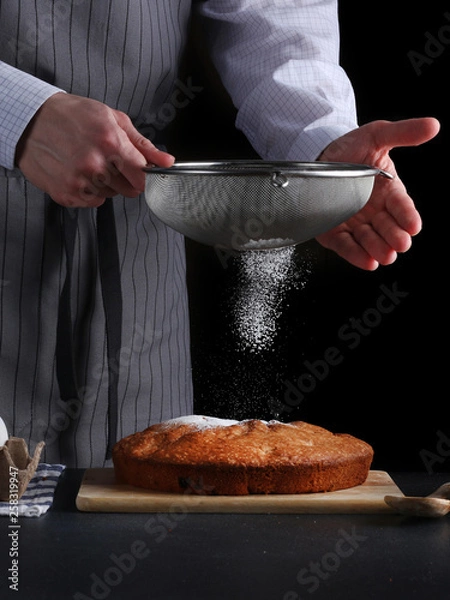 Fototapeta chef pouring powdered sugar on tasty pie on dark background. ched processing pie or cake