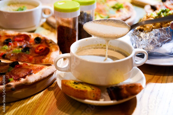 Fototapeta Bowl on a table with mushroom soup and a spoon hovering above