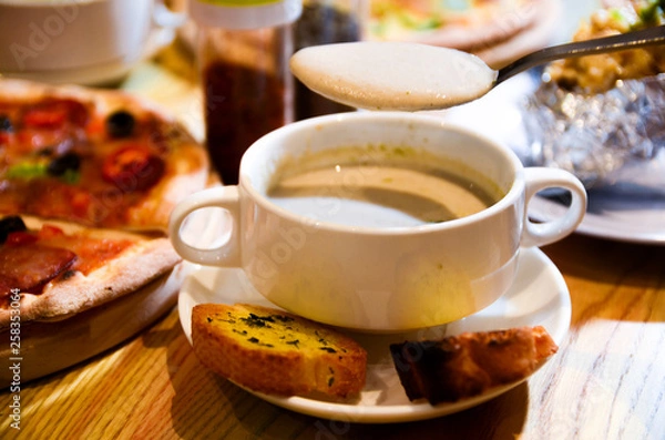 Fototapeta Bowl on a table with mushroom soup and a spoon hovering above