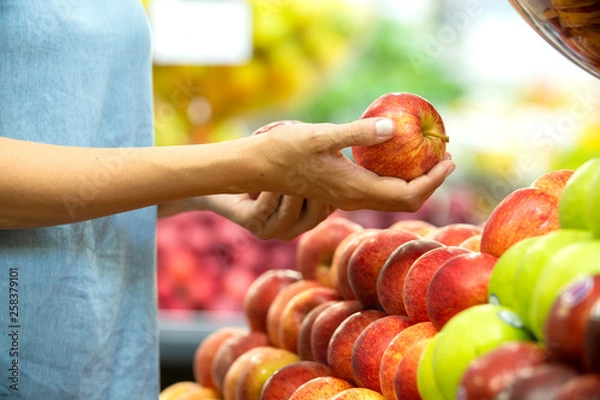 Fototapeta Woman's hand choosing red apple in supermarket