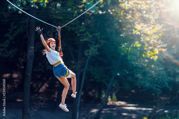 Fototapeta Szczęśliwe kobiety dziewczyna kobieta szybowcowa wspinaczka w ekstremalnych drogowych wózkach zipline w lesie na linku bezpieczeństwa karabińczyka na drzewie do parku linowego na szczycie drzewa. Koncepcja działań dla dzieci weekend rodzinny weekend