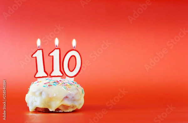 Obraz One hundred and ten years birthday. Cupcake with white burning candle in the form of number 110. Vivid red background with copy space