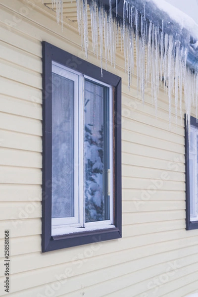Fototapeta Icicles hang from the roof of a private house in winter