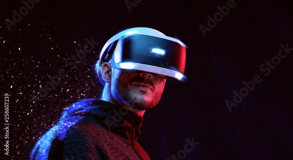 Obraz Model young man with beard in glasses of virtual reality on dark background.. Augmented reality, science, future technology concept. VR. Futuristic 3d glasses with virtual projection. Neon light.
