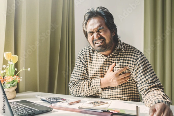 Fototapeta office syndrome concept; businessman sitting at office desk,  suffering from backache after working,man touching lower back with pained expression.