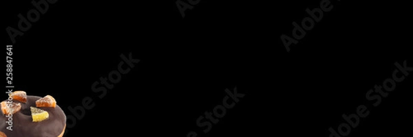 Fototapeta Appetizing donut with dark chocolate icing and marmalade decoration on a black background. Isolated. Banner.