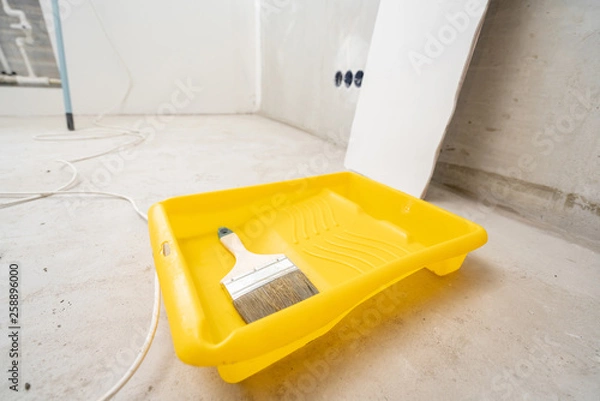 Fototapeta Paintbrush, roller and glue container on concrete surface. Composition tools for home repair and interior renovation indoors.