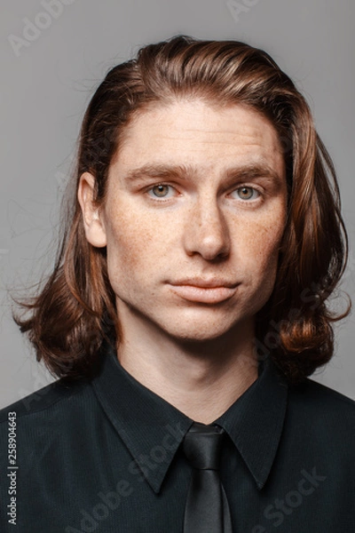 Obraz Portrait of a man with long hair and freckles, dressed in a black shirt and black tie