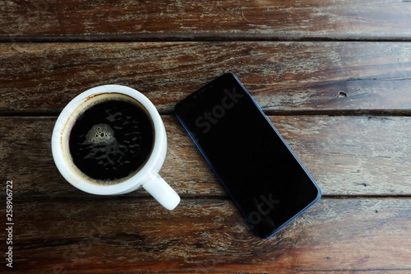 Fototapeta Flat lay photo of smartphone and black coffee on wood table with space for write wording, innovation that change the world such as communication way, business strategies, marketing strategies