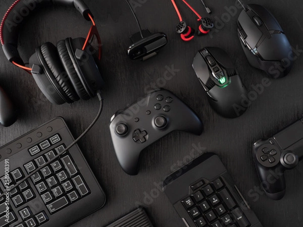 Fototapeta gamer work space concept, top view a gaming gear, mouse, keyboard, joystick, headset, mobile joystick, in ear headphone and mouse pad on black table background.