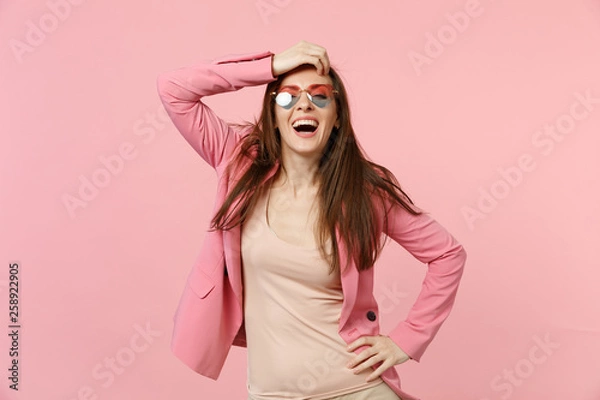 Fototapeta Portrait of stunning laughing pretty young woman in heart glasses putting hand on head isolated on pastel pink wall background in studio. People sincere emotions lifestyle concept. Mock up copy space.