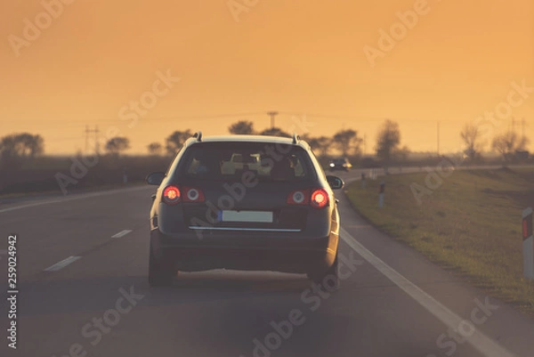 Obraz a black car drives towards the sunset